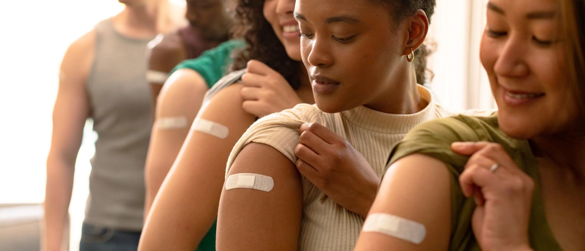 Group of diverse female and male friends showing plasters after vaccination