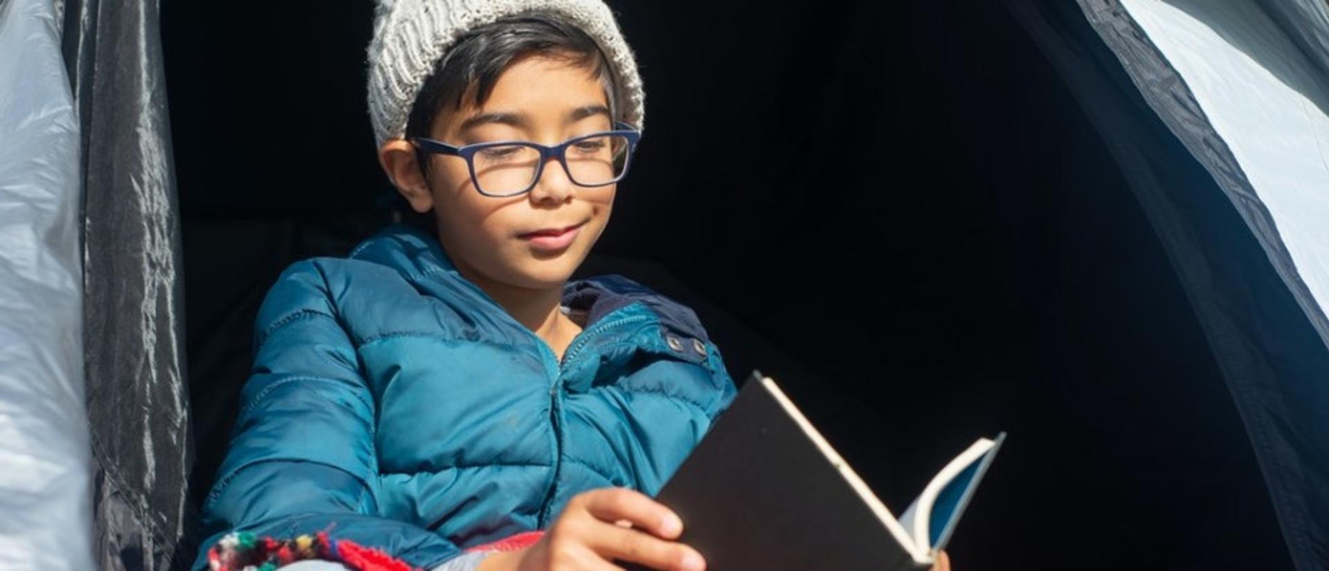 Boy in glasses reading in a tent