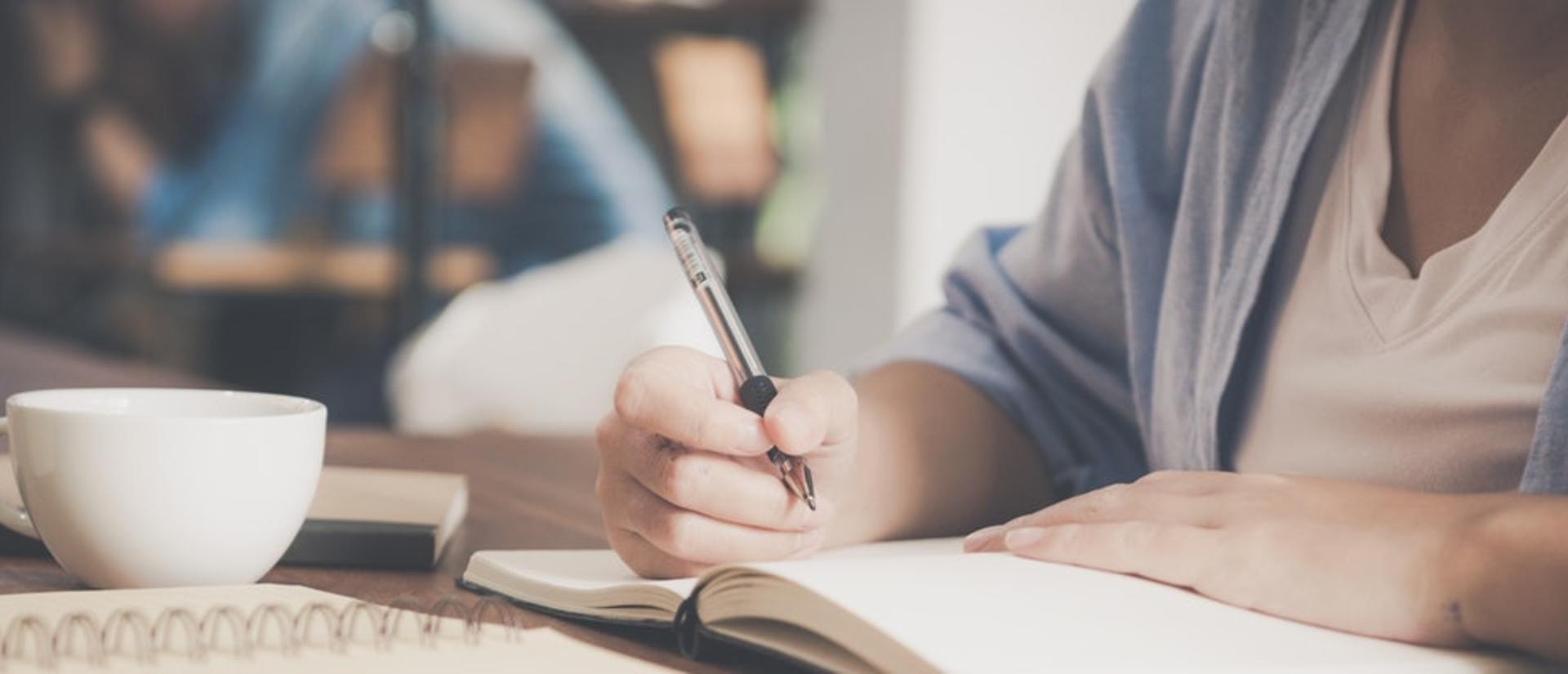 Woman writing on a notebook beside a teacup