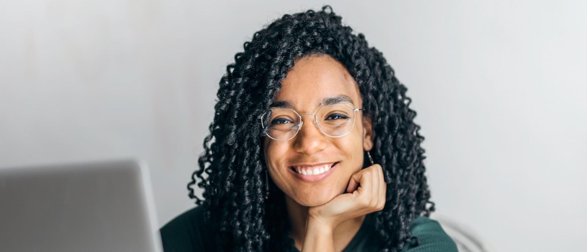 African-American woman using a laptop, looking at the camera and smiling.